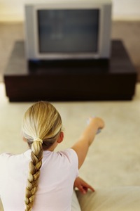 rear view of a girl pointing remote to a television