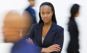 African-American businesswoman standing with arms crossed while others walk by.