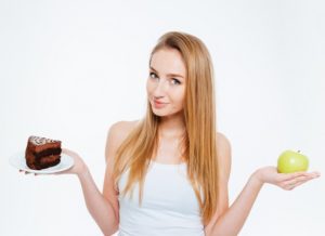 Attractive pretty young woman standing and holding healthy and unhealthy food over white background