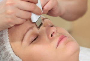 Woman under procedure of ultrasonic facial cleaning