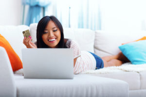 Happy asian woman shopping on-line while lying on the sofa