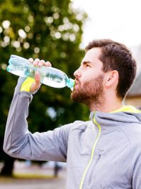 Close up of young hipster runner in town with water bottle, drinking