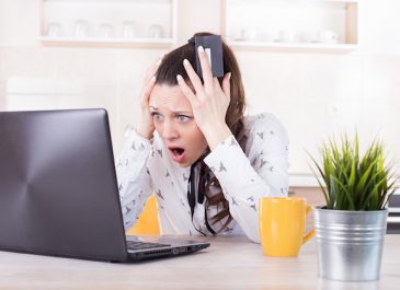 Shocked young woman holding credit card and looking at laptop. Negative surprise in e-banking