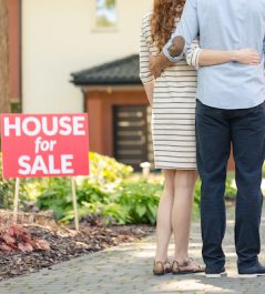 Back view of hugging couple standing with real estate agent in front of a house for sale