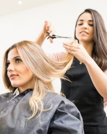 Pretty brunette working as a hairdresser and cutting hair tips of a female customer in a beauty salon