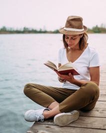 Portrait of a girl reading a book while sitting on a small wooden wharf.