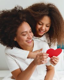 Mother and daughter enjoying on the bed, holding a heart