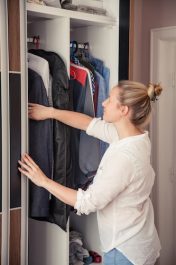 Caucasian woman is reaching for clothes from her closet.