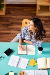 Smiling latin girl looking away while studying. Portrait of pensive college student looking away while studying alone at library. Young thinking woman taking notes at university.