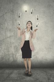 Full length of female entrepreneur juggling with light bulbs while standing with happy expression