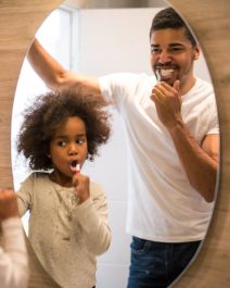 African american girl brushing teeth with dad.