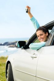 Woman driving car and holding keys on summer travel to coast. Happy female driver out of the window.