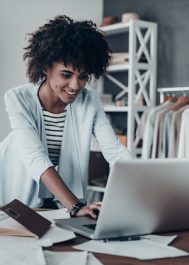 Beautiful young African woman working using computer and smiling while standing in workshop