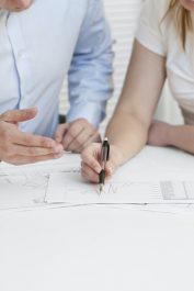 A businesswoman and a businessman in a meeting. Teamwork. Pointing and looking at a printed diagram on a table.